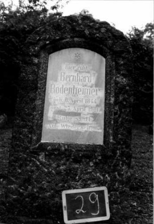 Grabstein 29 (Index: 100110445) Material: Granit mit weißer Marmorplatte Zustand: Schriftplatte gesprungen Maße HxBxT: 118x68x33 cm Beschreibung: grob stelenartig behauener Stein, Schriftplatte mit Segmentbogen Symbolik: sechszackiger Stern: Grabstein 29