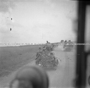Deutsche Soldaten auf einem Motorrad und LKW auf einer Landstraße, aus einem LKW fotografiert