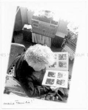 Blick auf eine alte Frau im Rollstuhl, die sich ein Fotoalbum anschaut (Sonderthema: Familienbilder)