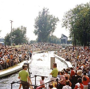 Hansjakob, Gottfried; Augsburg - Spickel, Am Eiskanal 30A; Kanuslalom Olympiastrecke, Freiflächengestaltung - Wettkampfstrecke während Olympiade, Tribünen vollbesetzt, im Hintergrund Pressegebäude, Blick Richtung Süden