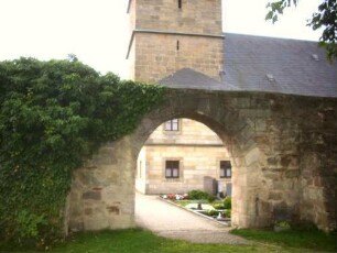 Ansicht von Norden im Nordosten mit Kirchturm (Schießscharten in den Mittelgeschossen) über Kirchhofmauer (Wehrgang mit Steinbrüstung im 18 Jh abgetragen) mit vereinfachtem Torbogen von Feldseite