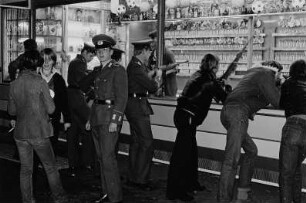 Jugendliche, teilweise in Uniform der NVA, an einem Schießstand auf dem Rummelplatz