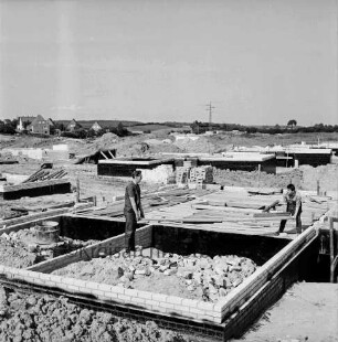 Schanzenbarg: Fundamente mit Grundmauern: vorn zwei Arbeiter mit Brett: dazwischen Ziegelstapel, Baumaterial und Erd- und Sandhaufen: hinten links zwischen Bäumen Wohnhäuser an Sehmsdorfer Straße