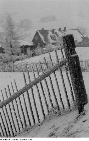 Aufnahme einer verschneiten Landschaft mit Holzzaun und Wohnhaus