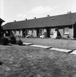 Tannenweg: Rentnerwohnblock: davor Frau: im Vordergrund Rasenfläche mit Plattenweg