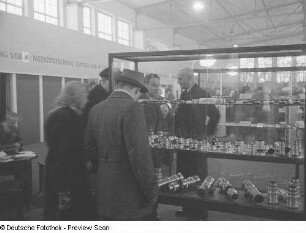 Messebesucher vor einer Vitrine mit Objektiven der Firma Meyer Optik