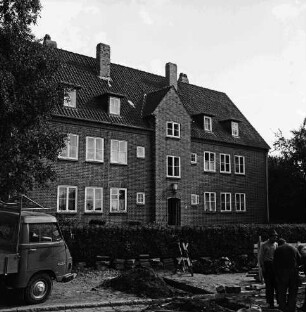 Hebbelstraße: Ausbau: vorn unbefestigte Straße, Erdhaufen, Absperrung, Stapel mit Gehwegplatten, Kleinlaster und zwei Arbeiter: dahinter Wohnhäuser der Gemeinnützigen Baugenossenschaft Bad Oldesloe mit Vorgärten