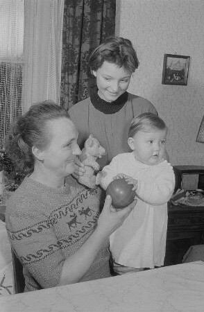 Zwei Frauen und ein mit Ball und Teddybär spielendes Kleinkind