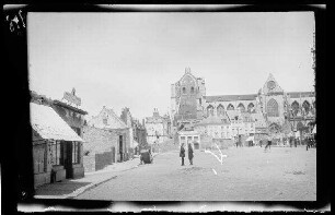 Löwen (Belgien): Stadtplatz mit Passanten, am Rand Ruinen einer Ladenzeile, im Hintergrund die zerstörte Kirche [Sint Pieter] (Distanzaufnahme) ("St. Pierre")