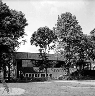 Stormarnhalle Bad Oldesloe: Am Bürgerpark: Blick von Osten: vorn Rasenfläche; links Gerüst; hinten Holzzaun und Bäume: hinten rechts Außentreppe: 20. Juni 1968