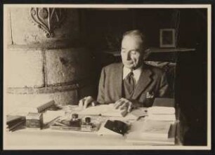 Der alte Rudolf Kassner am Schreibtisch mit Büchern und Tintenfässern, mit Widmung