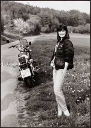 Frau steht in einer Wiese mit Motorrad (Altersgruppe 18-21)