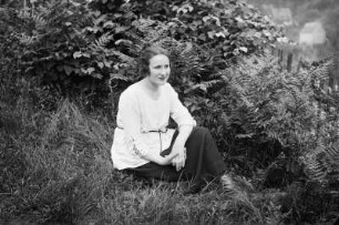 Portrait einer jungen Frau, auf der Wiese eines Gartens sitzend