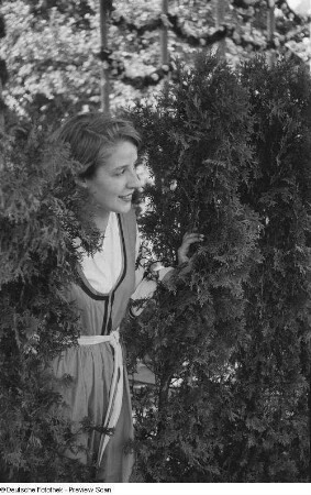 Junge Frau durch eine Hecke schauend