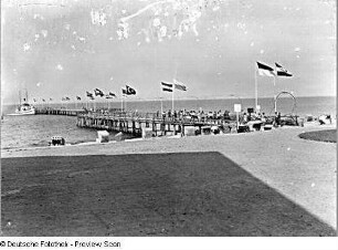 Blick über Ostseestrand zur Seebrücke mit Flaggen und Dampfer