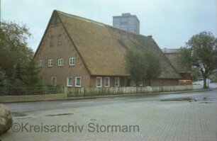 Wilstedt: Dorfring 159: traufständiges Bauernhaus mit Reetdach: Straßenfront mit Eingangstür: rechts Wirtschaftstrakt, auf Giebel Storchennest: links Wohntrakt und Giebelseite Wohntrakt: im Hintergrund Silo von Futterhandlung: von links Tangstedter Straße
