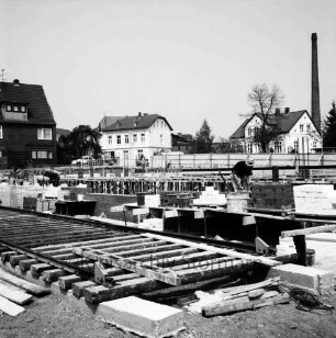 Käselau: Kaufhaus: Bahnhofstraße: in Bau: Kellergeschoss: Mauern, Gerüst, Bretter, Arbeiter: hinten Bauzaun: im Vordergrund Schienen für Baukran: hinten Häuser: im Hintergrund Schornstein