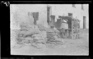 Bei Messines (=Mesen, Belgien), Wytsetate (=Wijtschate, Belgien),. Houthem (Belgien), Warneton (Dep. Nord, Frankreich) oder Loos (Dep. Nord, Frankreich): Sandsäcke, Wäscheleine und Bretterverschlag mit Bank und Tisch vor einer Hauswand