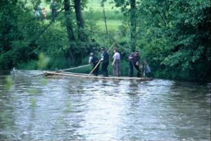 Floß mit Flößern und einer Frau am Ufer
