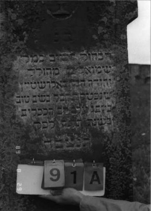 Grabstein 91 (Index: 100107298) Material: roter Sandstein Zustand: verwittert Maße HxBxT: 160x62x28 cm Beschreibung: Stele mit Giebel, Giebelfeld durch Medallion erhöht, Seitenakrotere, getreppter Sockel Symbolik: Levitenkanne: Grabstein 91A