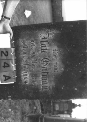 Grabstein 24 (Index: 99609660) Material: Sandstein Zustand: verwittert, Schrifttafel fehlt Maße HxBxT: 156x53x27 cm Beschreibung: Stele, Abschluß Sonderform, rechteckige eingelassene Schrifttafel fehlt, getreppter Sockel Symbolik: Vase mit zwei Zweigen: Grabstein 24A