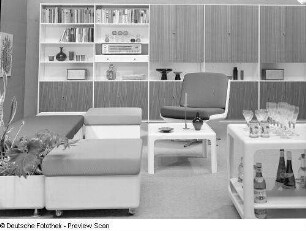 Vier Hocker und Drehstuhl mit Beistelltisch, Barwagen und Blumenkasten : Leipziger Herbstmesse, 1973. Möbelprogramm "variopur" (1973; VEB Petrolchemisches Kombinat Schwedt). Vier Hocker und Drehstuhl mit Beistelltisch, Barwagen und Blumenkasten vor Anbauwand