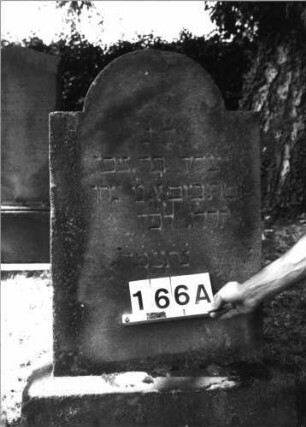 Grabstein 166 (Index: 100085419) Maße HxBxT: 100x56x13 cm Beschreibung: Stele, Sockel, eingezog. Rundbogenabschl. , Schriftfeld eingetieft auf Vorderseite: Grabstein 166A