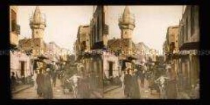 Belebte Straße mit Geschäften, Passanten, Fuhrwerk und Minarett