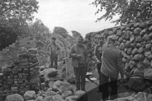 Gut Jersbek: Eiskeller: Restaurierung: Feldsteinmauer: Fachleute bei Begutachtung, im Beisein von Arbeitern: Feldsteine, Stapel mit Backsteinen: hinten Rest Backsteinmauer