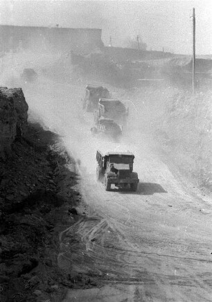 Lastkraftwagen beimTransport von abgebautem Erz auf staubiger Wegstrecke : Abbau von Erz in Rudny, der 1957 gegründeten Stadt