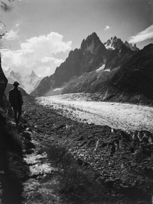 Am Gebirgspass : Blick über das Mer de Glace (Eismeer) auf einen Gebirgspass und den Aiguille des Grands Charmoz. Am Wegesrand steht ein Bergsteiger