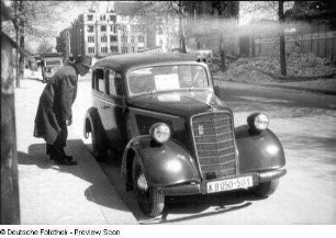 Berlin. Passant, offenbar Auskunft gebend, neben einem Personenkraftwagen "Opel" Super 6 (Baujahr 1936 ff) mit Kennzeichen für Berlin (KB für russisch 'Komendatura Berlin')