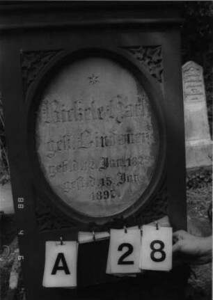 Grabstein 28 (Index: 99792857) Material: Sandstein und Marmor Zustand: Giebel stark verwittert Maße HxBxT: 164x52x31 cm Beschreibung: Stele, Sockel profiliert, Giebel mit Akroter, Schriftfeld eingetieft, stehendes Oval, eingesetzte Textplatte Symbolik: Efeublätter: Grabstein 28A