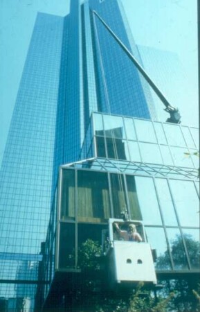 Frankfurt. Deutsche Bank. Ein Gebäudereiniger in der variablen Ein-Mann-Gondel bei der Arbeit an schrägen Glasflächen