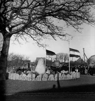 Ehrenmal mit Findlings-Einfriedung und Eiche: Einweihung mit Spalier der Freiwilligen Feuerwehr, Pastor Emil Lukas, Bürgermeister Heinrich Gehrke, seinem Stellvertreter Henry Barkmann, Gemeinderat Heinrich Behnk, Amtmann Heinrich Wolgast, Kreisamtmann Hans Bruhnsen und Kreisvorsitzender des Reichsbundes, Benno Uter: dahinter Gäste: Flaggenschmuck: im Hintergrund Bauernhäuser