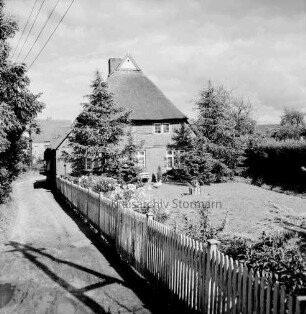 Reetdachhaus: rechts Garten mit Zaun: links Weg: hinten links weiteres Haus und Bäume