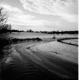 Trave: zugefrorener Fluss: links Baum: hinten Häuser: Winter