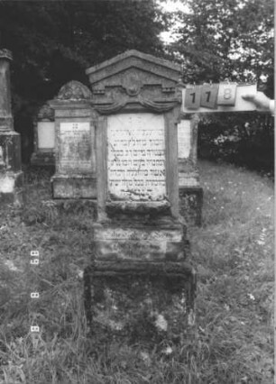 Grabstein 118 (Index: 99800082) Material: Sandstein, Schriftplatte Marmor Zustand: verwittert, Schriftplatte zersprungen Maße HxBxT: 154x46x21 cm Beschreibung: Stele, Giebel mit Verdachung, rechteckige eingelassene Schriftplatte, getreppter Sockel: Grabstein 118