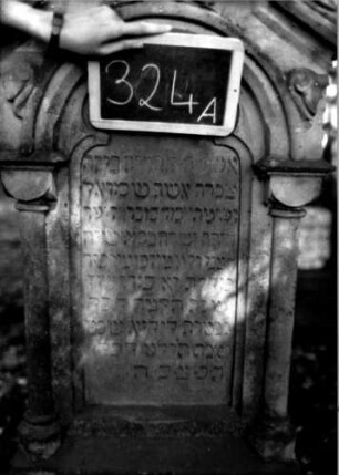 Grabstein 324 (Index: 100111970) Material: Sandstein Zustand: verwittert mit Textverlust Maße HxBxT: 164x62x32 cm Beschreibung: ädikulaartige Stele mit 3/4- Säulen, profilierter Sockel, schräg eingezogener Rundbogenabschluß mit Verdachung, Schriftfeld eingetieft Symbolik: Ranken, Rundbogenfries: Grabstein 324A