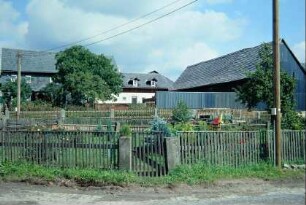 mit Staketenzäunen gesäumte Bauerngärten in der Ortsmitte, dahinter Hofanlage