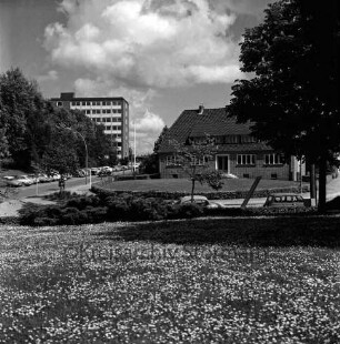Sülzberg: links Bangertstraße mit parkenden Pkws: dahinter Bäume und Hochhaus [später Gebäude B] der Kreisverwaltung: rechts Einmündung Bergstraße: dazwischen Gebäude: vorn Grünfläche des Kurparks mit Blumen, Baum und Pkws