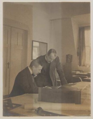Hofmannsthal und van de Velde über einen Tisch mit Zeichnungen gebeugt