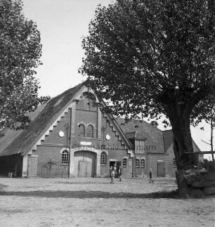 Hauptstraße: links und rechts Bäume: dahinter Bauerngehöft mit Wirtschaftsgebäude: im Hof spielende Kinder
