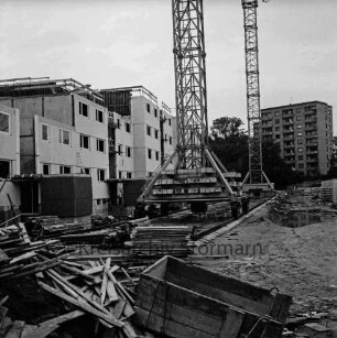 Am Kurpark: mehrgeschossiger Wohnungsbau: Rohbau: davor zwei Kräne auf Schienen: vorn Bauschutt, Bretter, Holzbalken: rechts Wasserpfütze und Baumaterial: dahinter Hochhaus am Sülzberg zwischen Bäumen