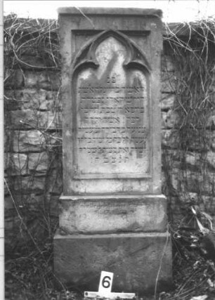Grabstein 6 (Index: 100105941) Material: Sandstein Zustand: leicht verwittert Maße HxBxT: 134x50x20 cm Beschreibung: rechteckige Stele, getreppter Sockel, Schriftfeld eingetieft mit Spitzbogenabschluß Symbolik: Maßwerk: Grabstein 6