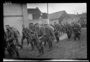 Metz-en-Couture (Dep. Pas-de-Calais, Frankreich): Soldaten mit Feldmützen, vorne umgehängtem Gewehr und Marschgepäck auf einer morastigen Ortsstraße