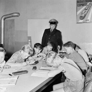 Hadamar (Landkreis Limburg-Weilburg). Wartesaal für Schulkinder (wohl im Bahnhofsgebäude). Kinder unter Aufsicht eines Bahnangestellten beim Erledigen der Hausaufgaben