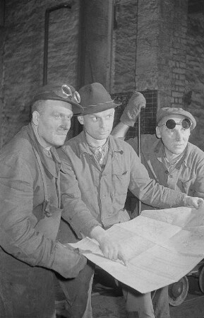 Drei Arbeiter des VEB Leipziger Eisen- und Stahlwerke zu Neujahr mit einem Plan in der Hand