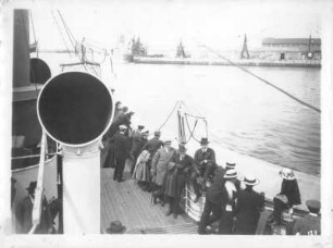 Kreuzfahrten der Hamburg-Amerika Linie, um 1911/1913. Touristen auf einem Zubringer-Dampfer bei der Ankunf in einem Hafen. Im Hintergrund Pier mit Schiffskränen und angelegtem Dampfer