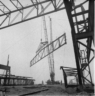 Zeithain. Baustelle Rohrwerk III des VEB Stahl- und Walzwerk Riesa. Stahlfachwerkbinder einer Produktionshalle am Kranhaken, mit Traverse angeschlagen
